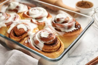 Beyaz mermer arka planda kremalı lezzetli tarçınlı rulo pişirme yemeği, yakın plan.