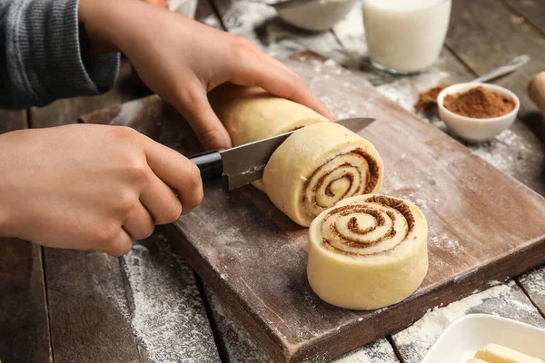 Ahşap arka planda lezzetli tarçınlı rulo hazırlayan kadın.