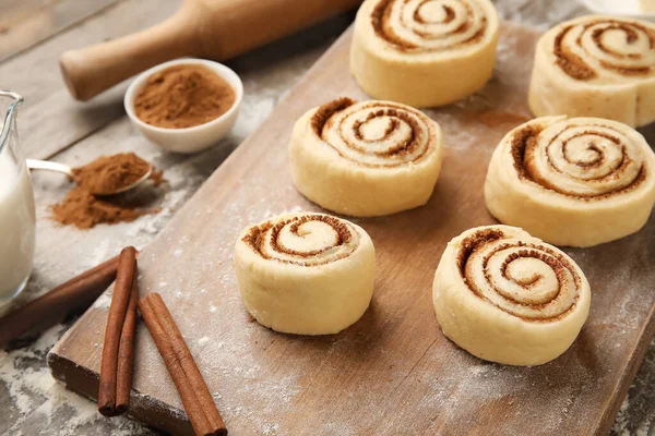 Ahşap arka planda pişmemiş tarçın ruloları olan tahta, yakın plan.