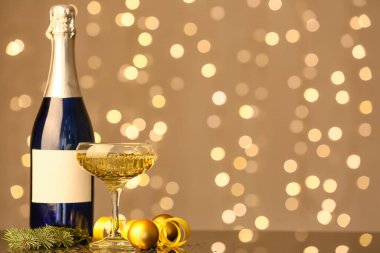 Bulanık arka planda Noel dekoru olan bir şişe ve bir bardak şampanya.