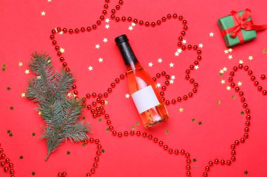 Kırmızı arka planda bir şişe şampanya ve Noel dekoru olan kompozisyon