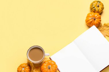 Bir fincan lezzetli kahve, boş kitap ve sarı arka planda balkabakları.