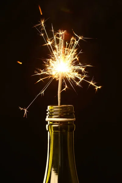 Bottle of champagne with Christmas sparkler on black background, closeup