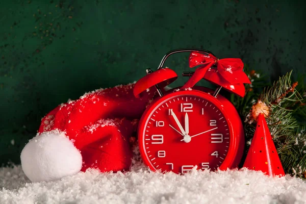 Komposition Mit Weihnachtswecker Und Weihnachtsmütze Auf Schnee Vor Grünem Hintergrund — Stockfoto