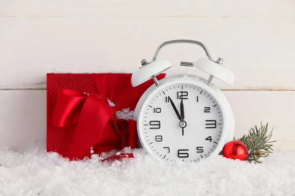 光の木製の背景に雪の上の目覚まし時計とクリスマスプレゼント — ストック写真