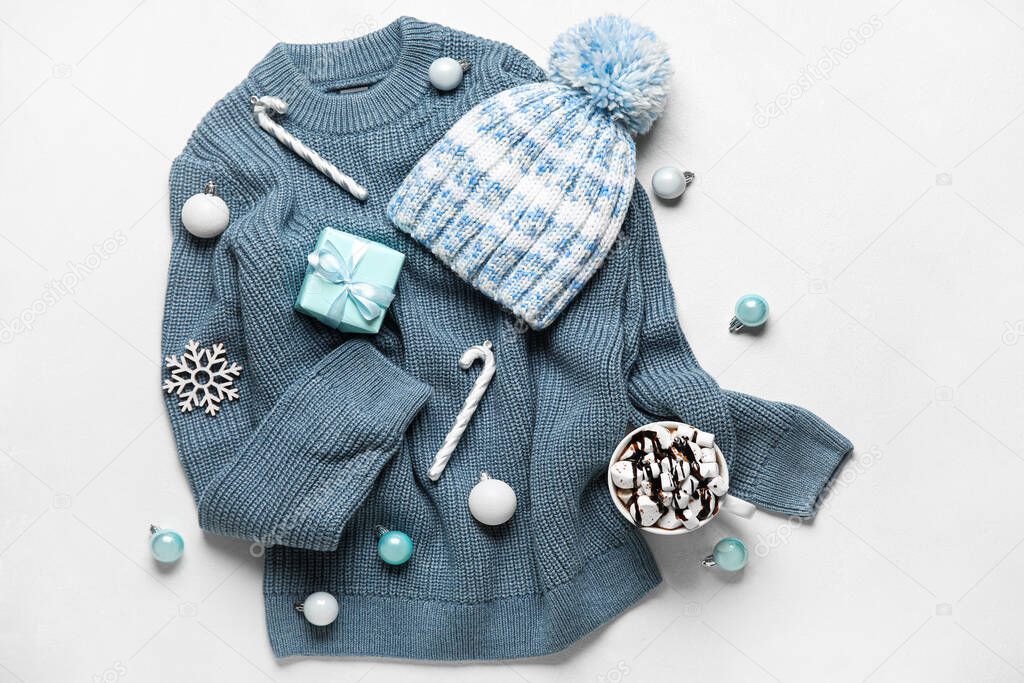 Warm sweater, hat, Christmas decor and cup of hot chocolate on light background