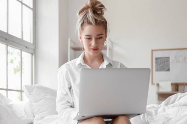 Yatakta dizüstü bilgisayar kullanan güzel bir genç kadının sabahı.