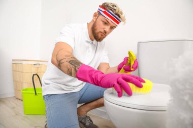 Tuvaleti süngerle temizleyen genç bir adam.