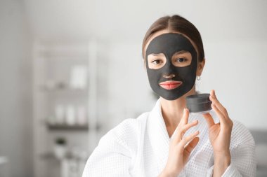 Evde yüzünde aktif kömür maskesi olan genç bir kadın.