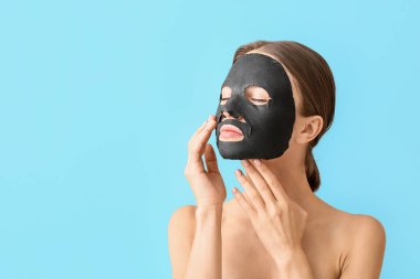 Yüzünde renkli kömür maskesi olan genç bir kadın.