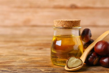 Bir şişe gerekli yağ ve ahşap arka planda taze kestaneler, yakın plan.