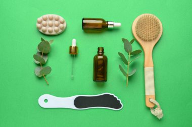Temel yağ şişeleriyle kompozisyon, masaj için ayak dosyası, sabun ve yeşil arka planda masaj fırçası