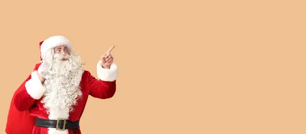 Święty Mikołaj Torbą Wskazującą Coś Beżowym Tle Miejscem Tekst — Zdjęcie stockowe