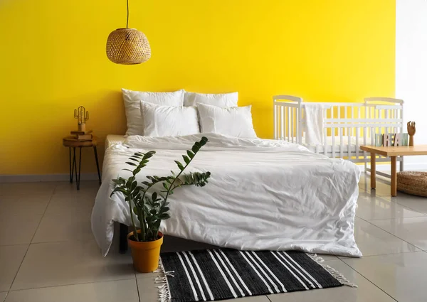 部屋の中で黄色の壁の近くに白いベビーベッド付きの大きな快適なベッド — ストック写真