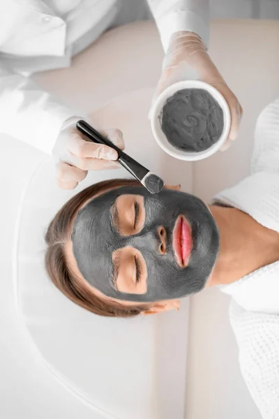 Kosmetikerin Trägt Aktivkohlemaske Schönheitssalon Auf Das Gesicht Der Frau Auf — Stockfoto