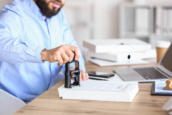 Нотариус-мужчина, прикрепляющий печать к документам в офисе