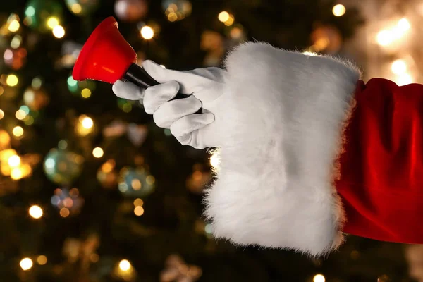 Santa Ręka Dzwonkiem Świątecznym Przed Rozmytymi Światłami — Zdjęcie stockowe