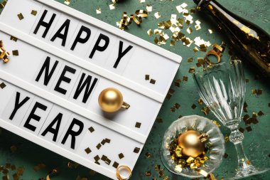 Mutlu Yıllar yazılı pano, şampanya şişesi, gözlük ve yeşil arka planda Noel dekoru, yakın plan.