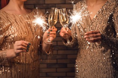 Şampanya kadehleri ve duvarda Noel ışıkları olan genç kadınlar, yakın plan.