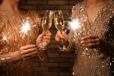 Şampanya kadehleri ve duvarda Noel ışıkları olan genç kadınlar, yakın plan.