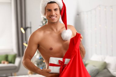 Noel Baba çantasıyla dolu seksi genç adam yatak odasında.