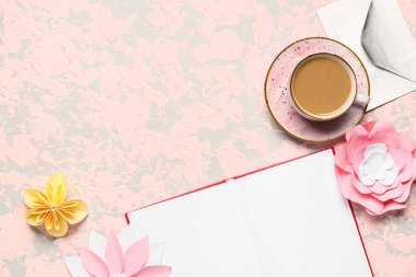 Bir fincan lezzetli kahve, boş kitap ve bej arka planda kağıt çiçekler.