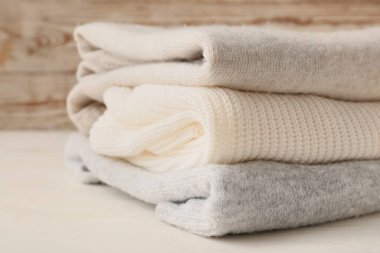 Hafif ahşap arka planda farklı rahat süveterler yığını, yakın plan.