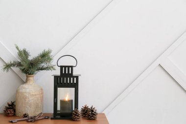 Yanan mum, vazo, köknar dalları ve koni ışığın yanındaki masada duran siyah Noel feneri.