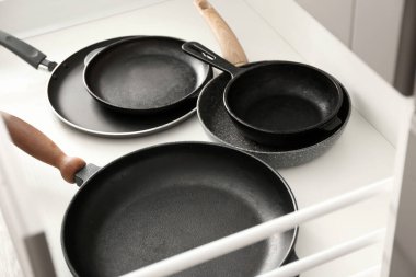 Açık mutfak çekmecesinde farklı kızartma tavaları, yakın çekim.