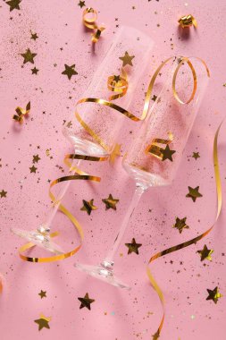Şampanya bardaklı kompozisyon, pembe arka planda yılan yağı ve konfeti.