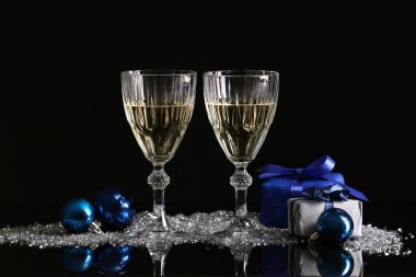 Şampanya kadehleri, Noel süslemeleri ve karanlık arka planda hediye kutuları.