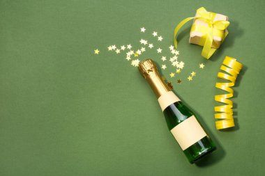 Yeşil arka planda bir şişe konfeti ve hediye.