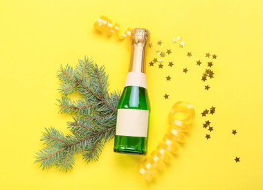 Sarı arka planda bir şişe şampanya ve Noel dekoru olan kompozisyon