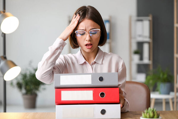 Стрессовая молодая женщина, работающая с документами в офисе