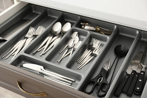 Open drawer with silver cutlery in modern kitchen, closeup