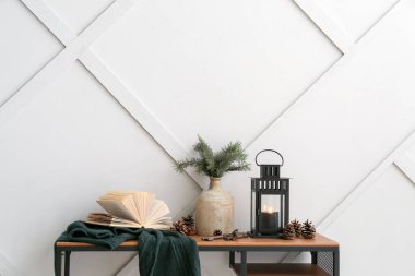 Yanan mum, vazo, köknar konileri ve ışık duvarının yanındaki masada kitap olan siyah Noel feneri.