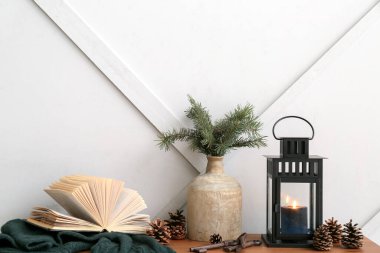 Yanan mum, vazo, köknar konileri ve ışık duvarının yanındaki masada kitap olan siyah Noel feneri.