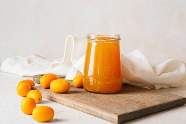 Bir kavanoz lezzetli kumkat reçeli ve hafif arkaplanda taze meyveler.