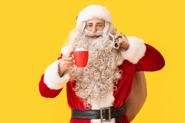 Santa Claus Filiżanką Gorącego Kakao Worek Żółtym Tle — Zdjęcie stockowe