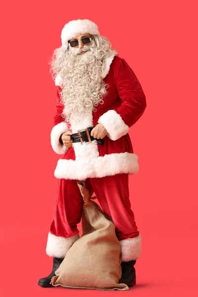 Święty Mikołaj Okularach Przeciwsłonecznych Workiem Czerwonym Tle — Zdjęcie stockowe