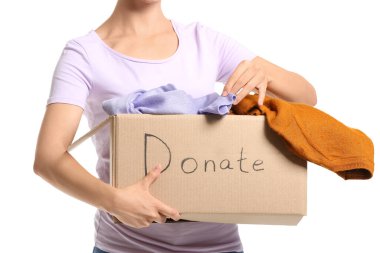 Beyaz arka planda bağış giysileri olan bir kutu tutan genç kadın.