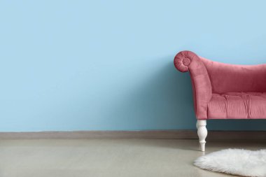 Mavi duvarın yanında zarif pembe koltuk ve kabarık halı.