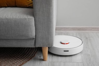 Odadaki kanepenin yanındaki modern robot elektrikli süpürge.