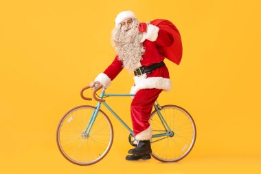 Sarı arka planda çantası ve bisikleti olan Noel Baba.