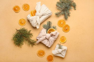 Kumaşa sarılı Noel hediyeleri, köknar dalları ve arka planda kurutulmuş portakal dilimleri içeren kompozisyon