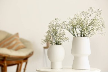 Oturma odasındaki masada çingene çiçekli beyaz vazolar.
