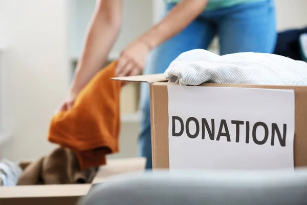 Cardboard box with clothes for donation in room, closeup