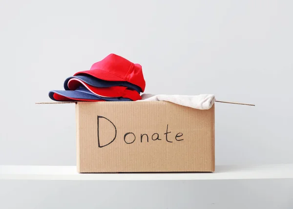 Cardboard box with donation clothes on shelf against light background