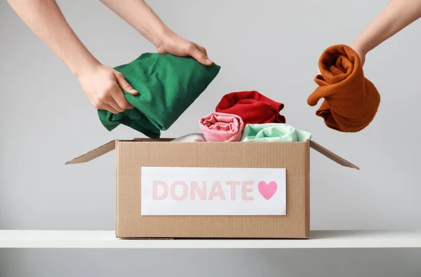 Women putting donation clothes in box on shelf against light background