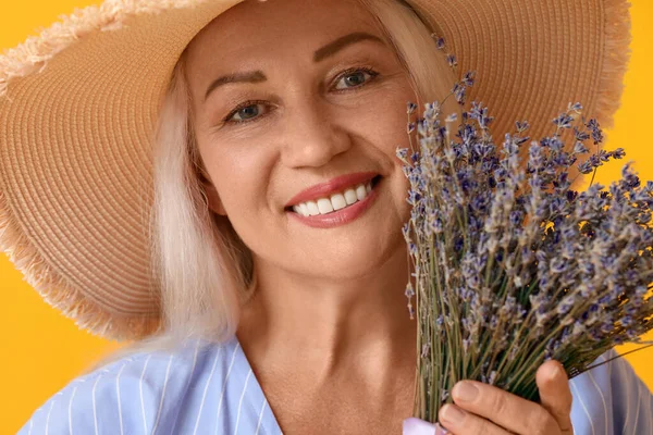 Hasır şapkalı, elinde bir buket çiçekle gülümseyen olgun bir kadın.